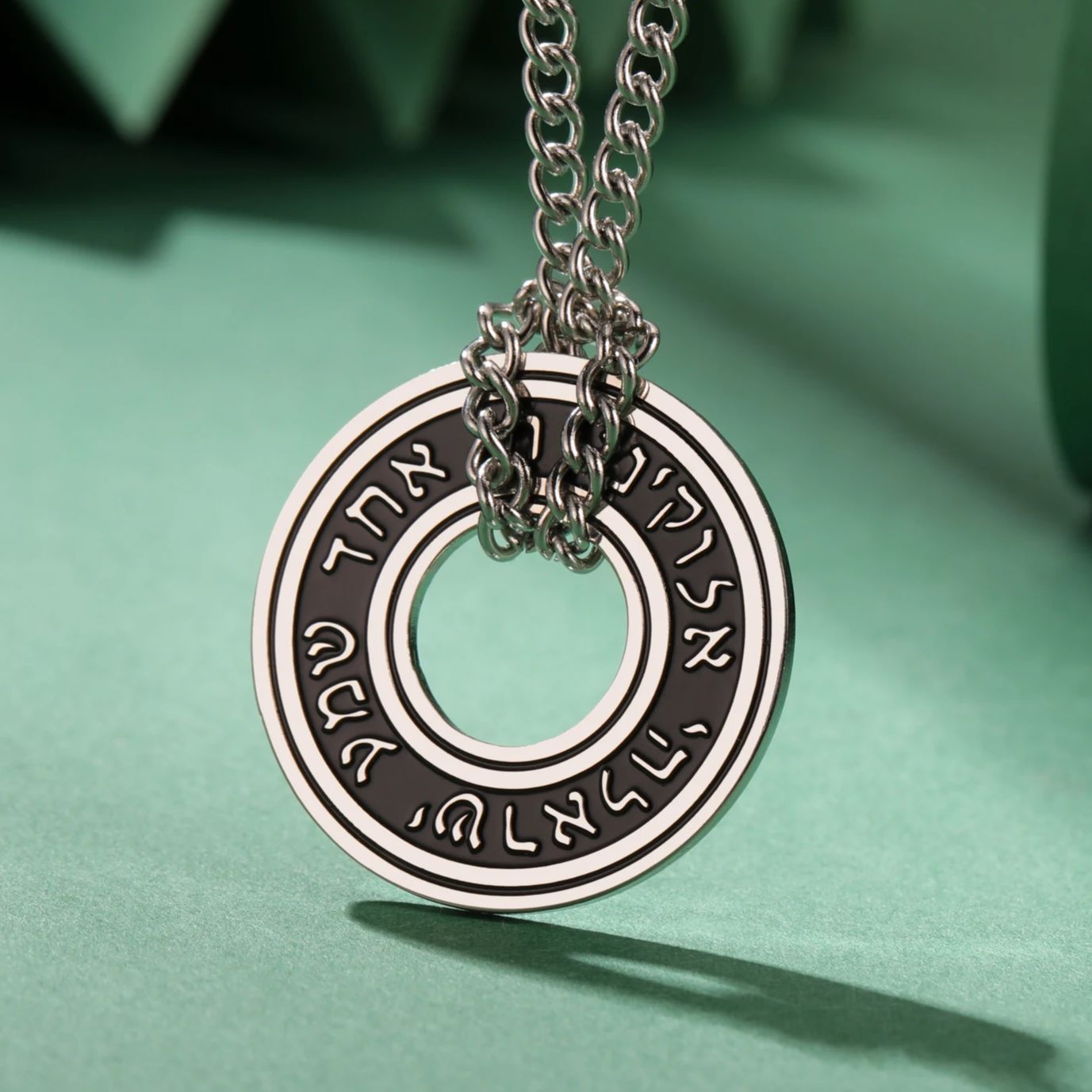 Collier rond argenté avec inscription hébraïque et chaîne métallique, style judaïca discret.
