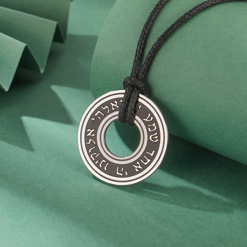 Pendentif rond en acier inoxydable avec inscription hébraïque, monté sur cordon noir réglable.