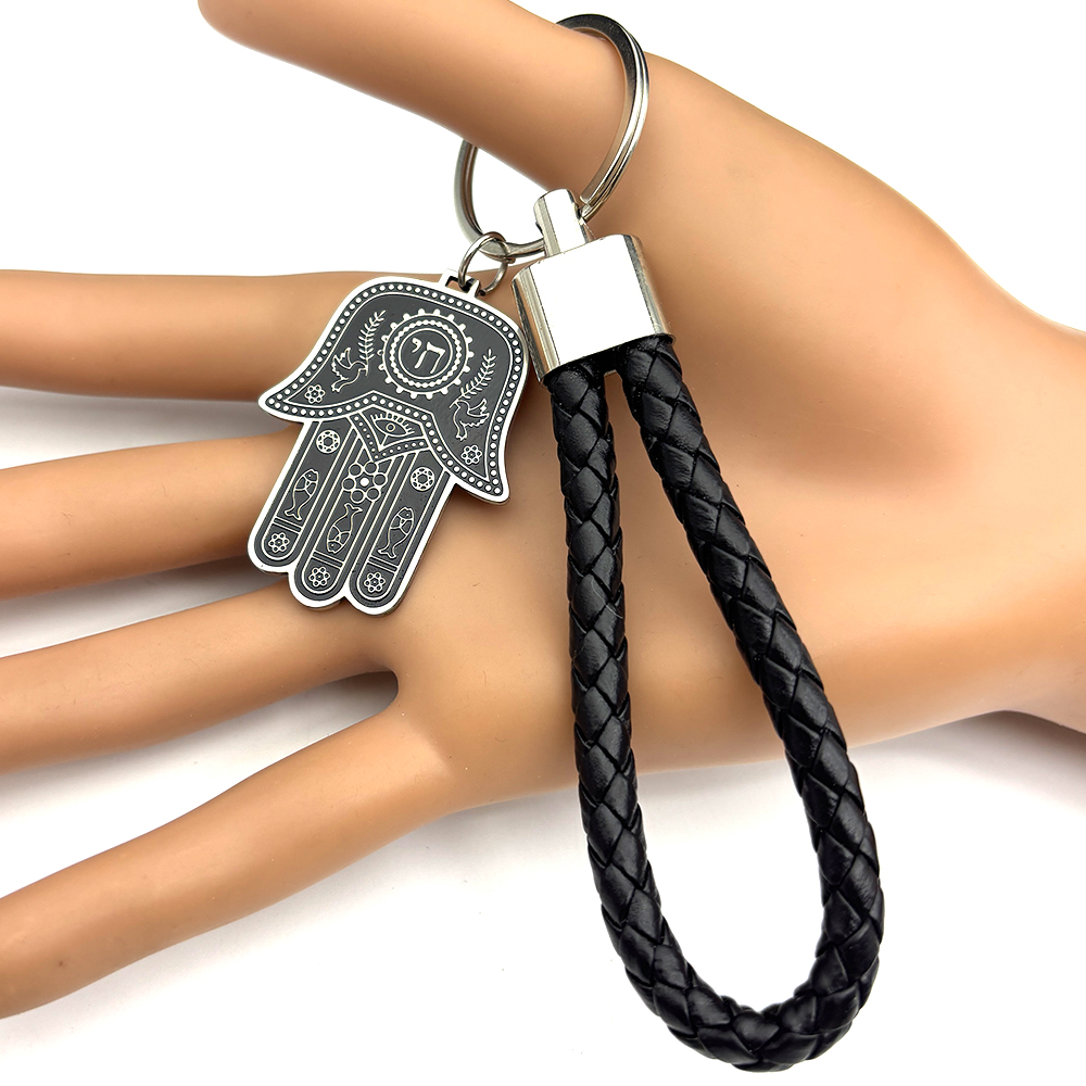 Porte-clés Hamsa en acier inoxydable avec cordon noir tressé et détails hébraïques.