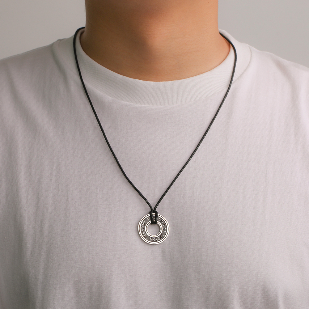 Pendentif rond en acier inoxydable avec inscription hébraïque, monté sur cordon noir réglable.
